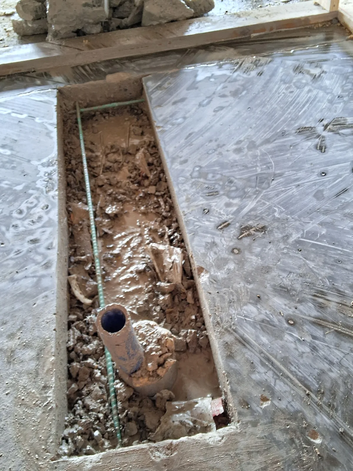 Flat-sawn trench opened in a concrete slab exposing drain pipe