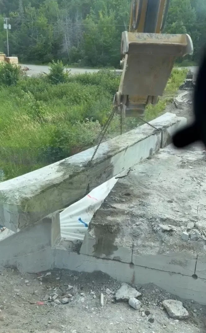 Excavator removing a wire-sawn concrete bridge beam