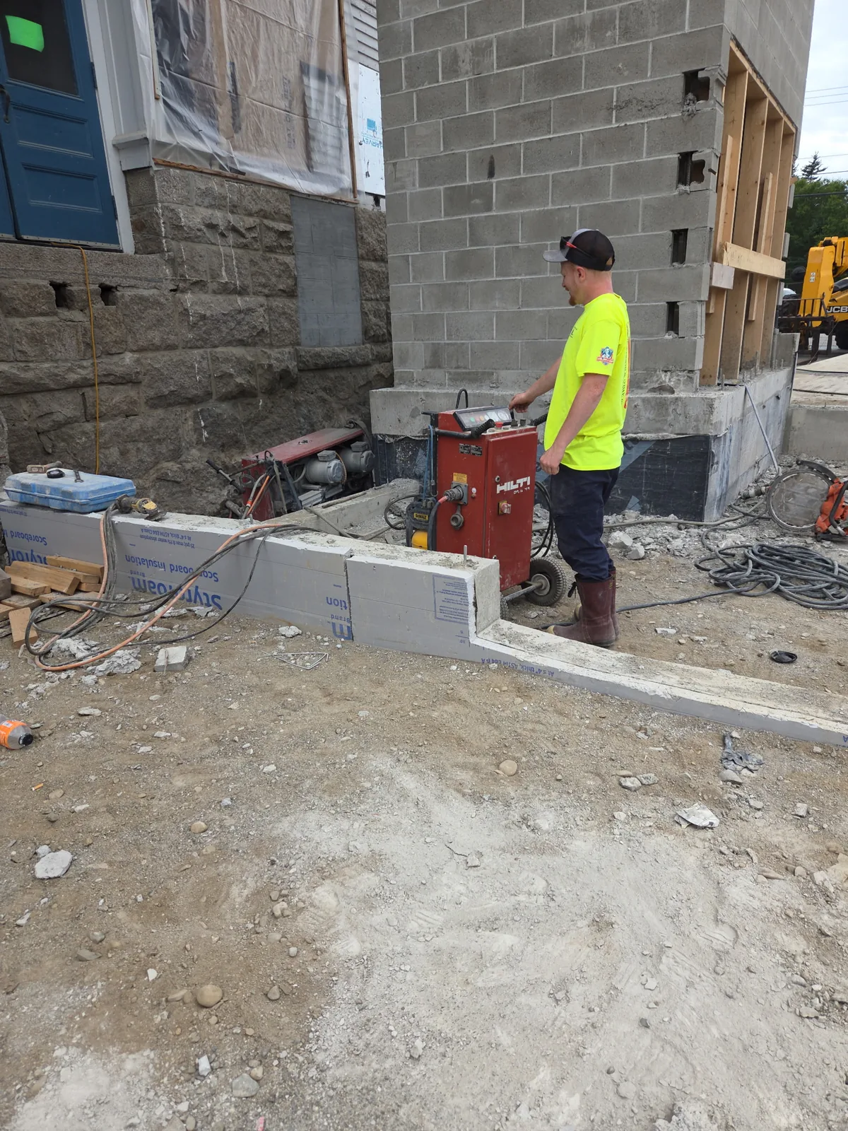 Operator wire sawing a concrete foundation section at a building addition